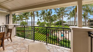 A covered outdoor area with a stone floor, a wooden chair, and a view of a well-maintained lawn and palm trees. - Turtle Bay Villas 307 by Gather: Beachfront w/ Shared Pool/Spa/AC (Kahuku)