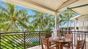 A balcony with a wooden table and chairs, overlooking a pool and palm trees. - Turtle Bay Villas 310 by Gather: Beachfront w/ Shared Pool/Spa/AC (Kahuku)