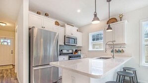 Una cocina moderna con armarios blancos, electrodomésticos de acero inoxidable y una isla central con taburetes.