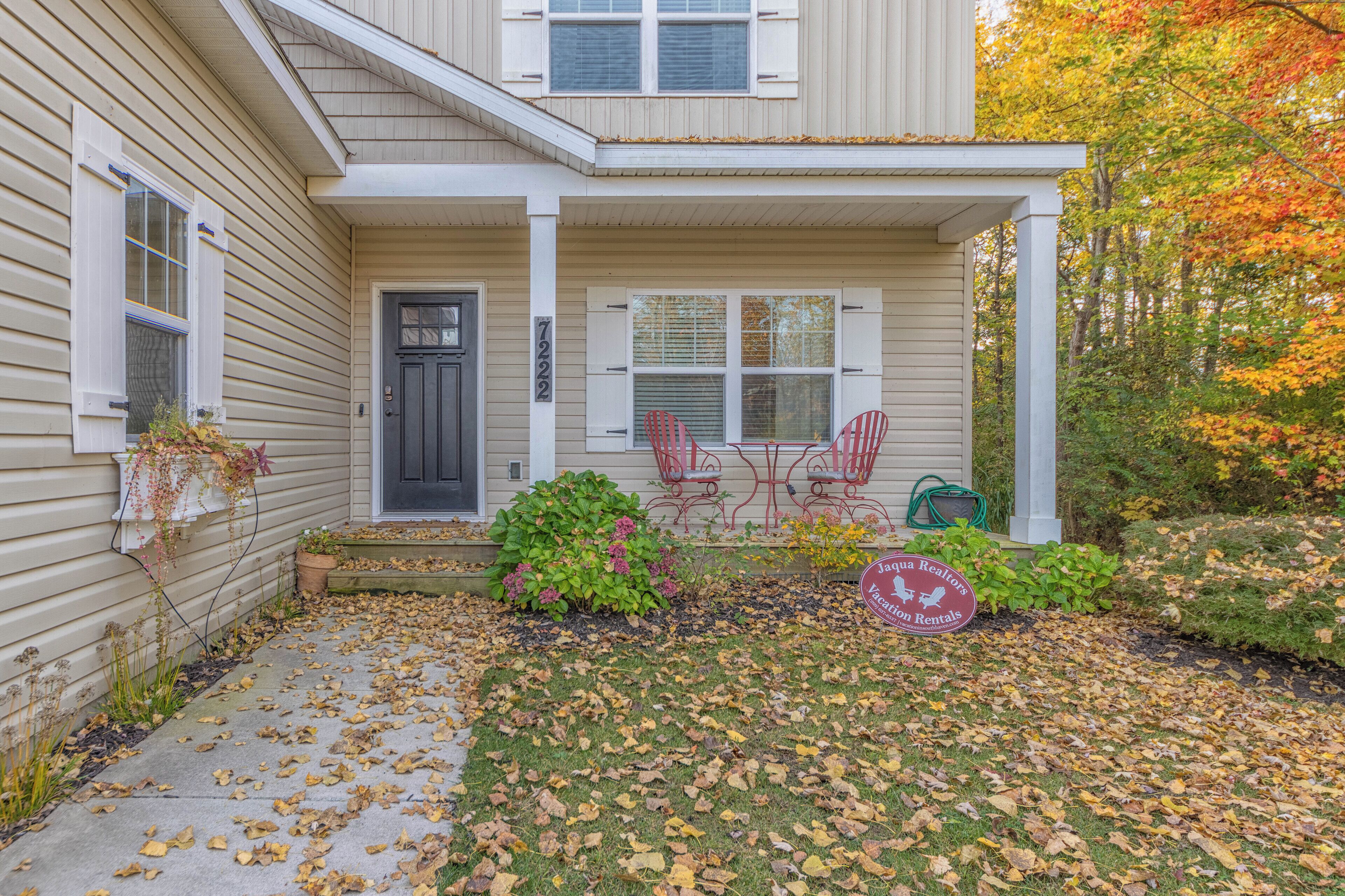 A two-story house with a front porch, a black door, and a patio area with red chairs.
