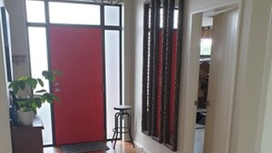 Un pasillo con suelo de madera, una puerta roja, un ventilador de techo y una planta en maceta.