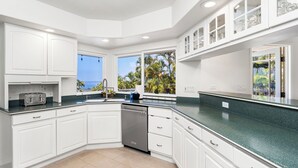 Een moderne keuken met witte kasten, een vaatwasser en uitzicht op palmbomen.