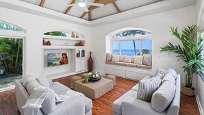 Een ruime woonkamer met een hoge plafond, inbouwkasten, een groot raam met uitzicht op zee, en een zithoek met een salontafel.