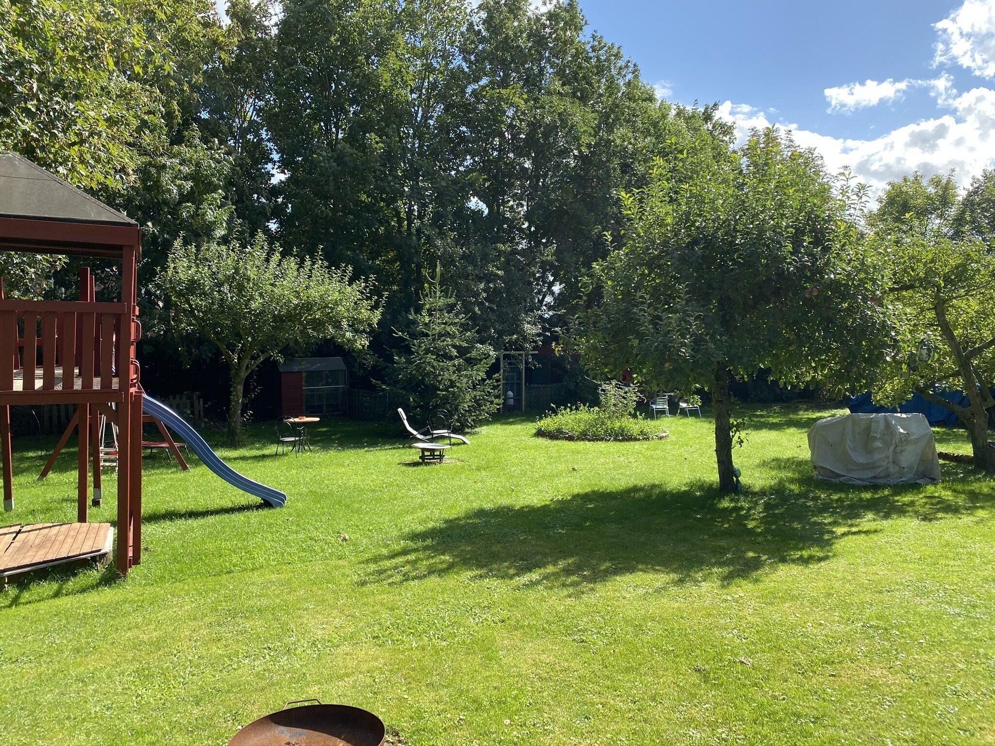 Ein Garten mit Rasenfläche, einer hölzernen Spielanlage, einer Rutsche und einer überdachten Sitzgelegenheit.