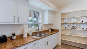 Una cocina con armarios blancos, encimera de granito, un fregadero y una ventana con persianas.
