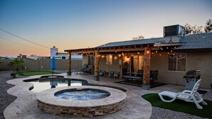 Un patio trasero con jacuzzi, mobiliario exterior y un porche cubierto.