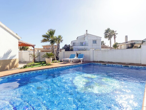 A swimming pool with two lounge chairs, surrounded by a white wall and palm trees. - Estrella by Interhome (Deltebre)