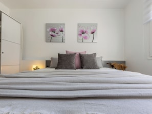 Un dormitorio con cama, almohadas y dos cuadros de flores colgados en la pared.