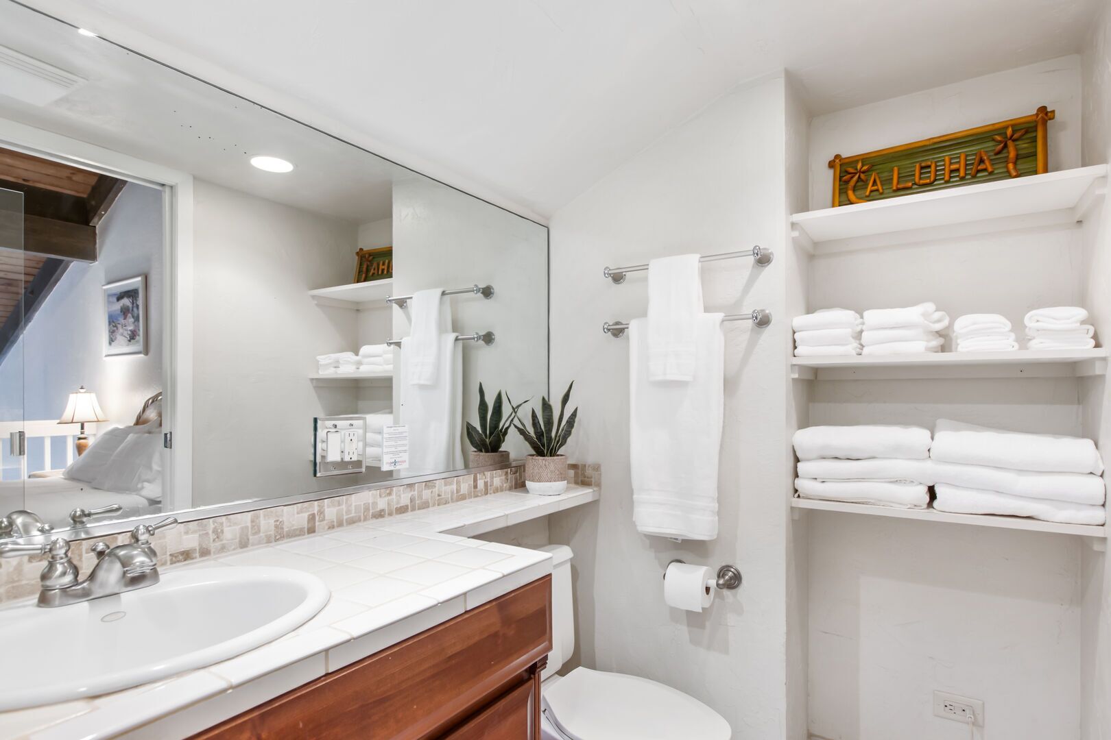 Un baño moderno con un espejo grande, dos lavamanos, un inodoro y un estante con toallas dobladas.