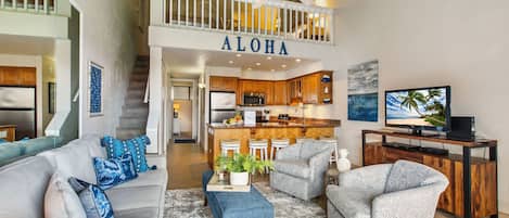 A spacious living area with a high ceiling, a kitchen with wooden cabinets, and a balcony with a railing.
