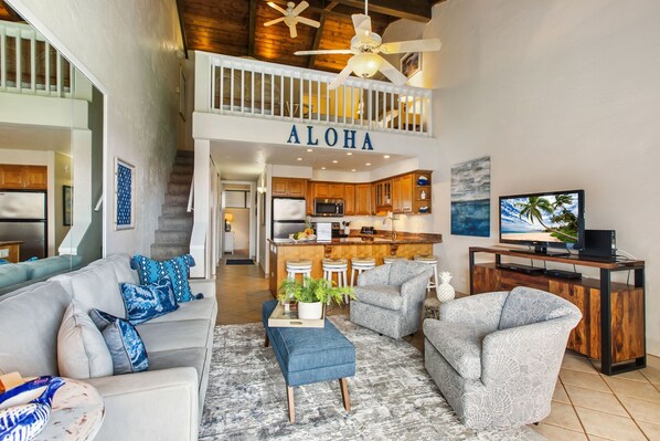 A spacious living area with a high ceiling, a kitchen with wooden cabinets, and a balcony with a railing.