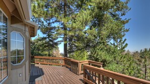 A wooden deck with railings, surrounded by tall pine trees.