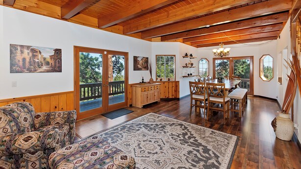 A spacious room with wooden beams, a dining area, and large windows.