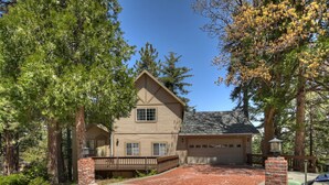 A two-story house with a garage, surrounded by tall trees and a brick driveway.