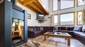 A living room with a fireplace, leather sofas, a coffee table, and large windows. - Spacious chalet La Tania, with half-board (la perriere)