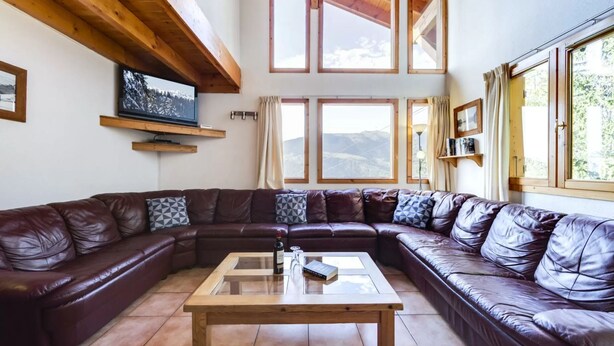 A cozy living room with a large L-shaped leather sofa, a wooden coffee table, and a TV mounted on the wall. - Spacious chalet La Tania, with half-board (la perriere)