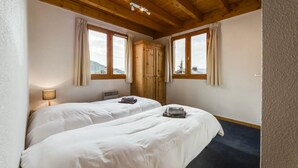 A room with two beds, wooden ceiling beams, large windows with curtains, and a view of the outdoors. - Spacious chalet La Tania, with half-board (la perriere)