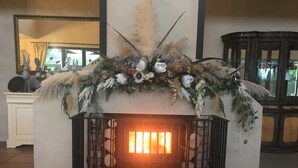 A fireplace with a decorative mantel, flanked by black metal railings, in a room with a tiled floor and a large mirror on the wall.