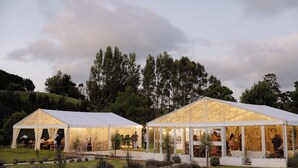 Two large, white tents with glass walls, set on a grassy field with trees in the background.