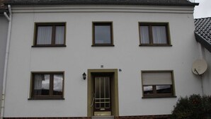 A two-story building with a white facade, a central entrance with a door, and four windows on the upper floor.