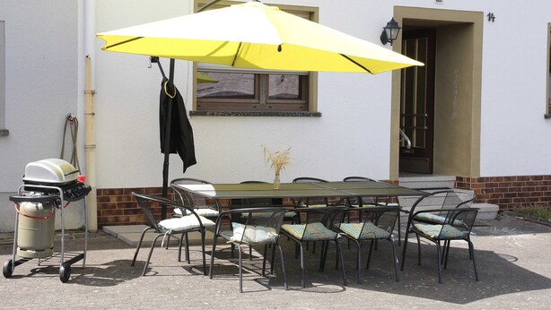 An outdoor dining area with a table and chairs, a yellow umbrella, and a grill cart.