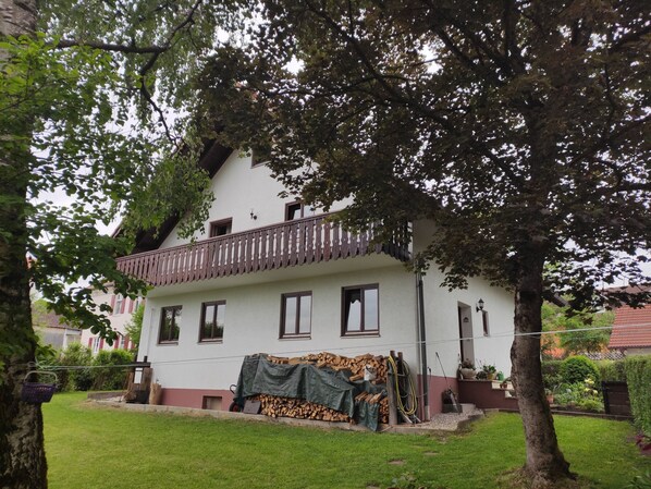 Ein zweistöckiges Haus mit Balkon, Rasen und Holzstapel.