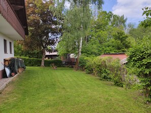 A well-maintained garden with a lawn, trees, and a building with a balcony.