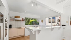 A modern kitchen with white cabinetry, a central island, and a view of greenery outside.