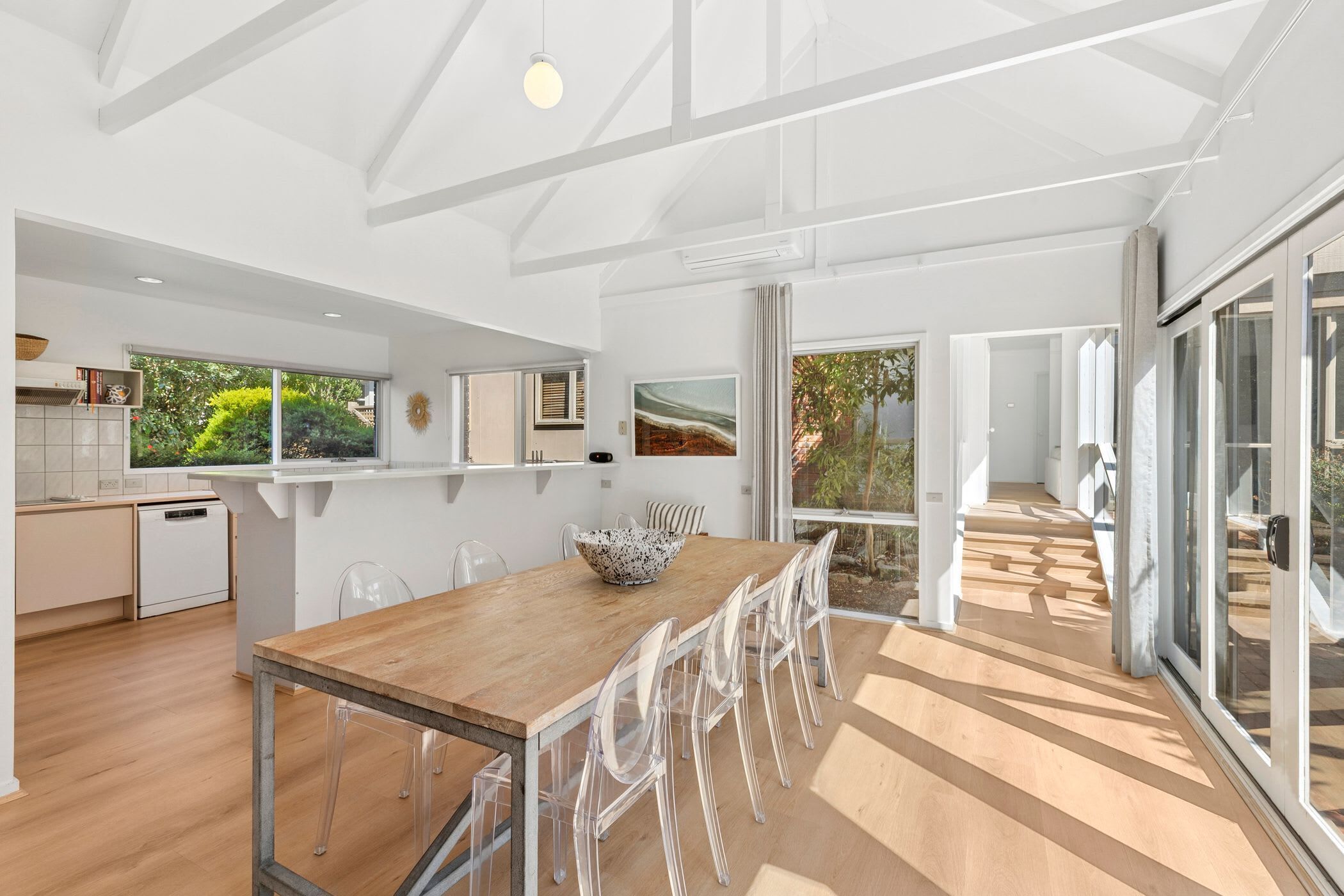 A modern kitchen with a wooden table and chairs, a dishwasher, and a view of greenery outside.