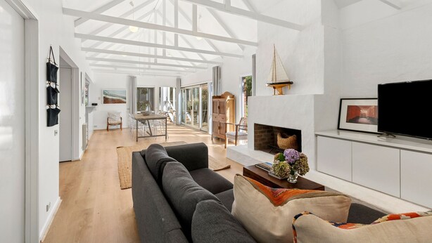 A spacious living area with a large sofa, a fireplace, and a television. There is a dining area in the background with a table and chairs.