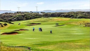 A golf course with bunkers, a clear sky, and distant hills.