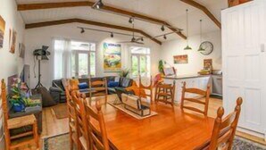 A dining area with a wooden table and chairs, a sofa, and a kitchen area with a refrigerator and sink.