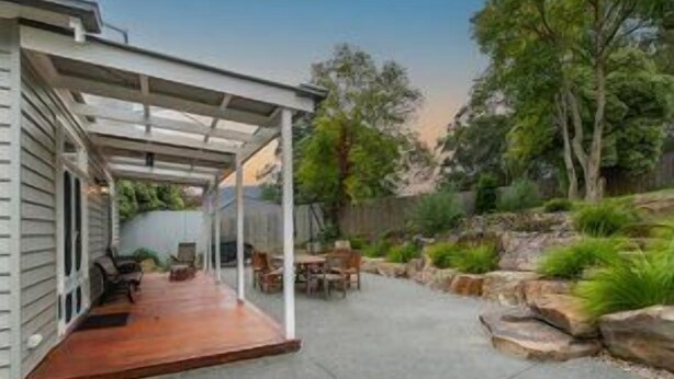 A covered patio area with outdoor furniture, a stone retaining wall, and surrounding greenery.