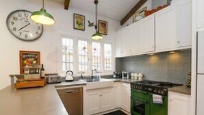 A kitchen with white cabinets, a green stove, a clock, and a window with a view of the outside.