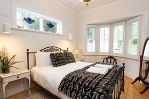 A bedroom with a bed, a nightstand, a window with blinds, and a wall-mounted shelf with decorative items. - Vintage Charm on St Leonards in the Yarra Valley (Yarra Ranges)