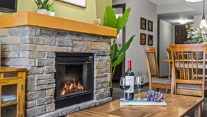 A stone fireplace with a fire, a dining table with wine glasses and grapes, and a wooden chair.
