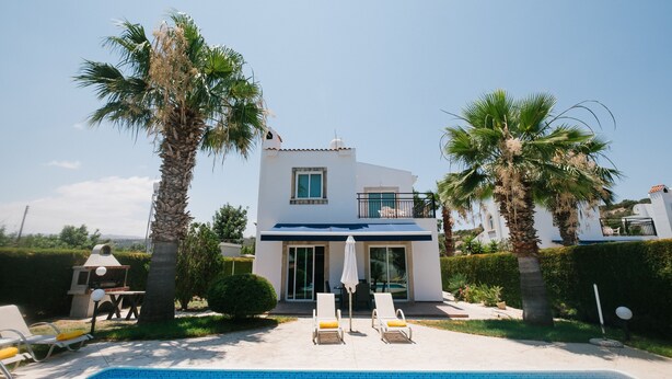 A modern two-story house with a swimming pool, palm trees, and a patio with lounge chairs. - Cleopatra Villa (Neo Chorio)