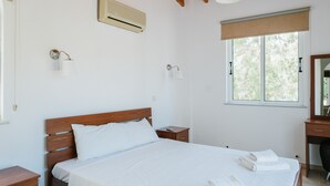 A bedroom with a wooden bed, bedside tables, a desk, and a window with a view of trees. - Cleopatra Villa (Neo Chorio)