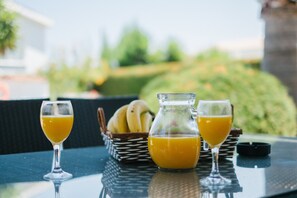 Una mesa con dos vasos de jugo de naranja, una cesta de mimbre con plátanos y una jarra de vidrio con jugo de naranja.