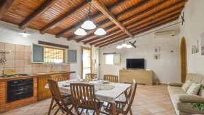 A spacious kitchen with wooden beams, a dining area with a table set for four, a television, and a sofa in a living area. - Lovely home in Castelvetrano (Castelvetrano)