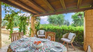 An outdoor patio with a round table set for dining, surrounded by chairs, under a wooden pergola. - Lovely home in Castelvetrano (Castelvetrano)