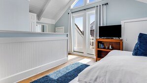 A bedroom with a large bed, a television on a wooden stand, and a view of the outside through a sliding door.