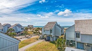 A coastal residential area with houses featuring a uniform architectural style, a clear view of the ocean, and a well-maintained lawn.
