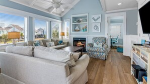 A spacious living room with a large sofa, a patterned armchair, a fireplace, and a television.