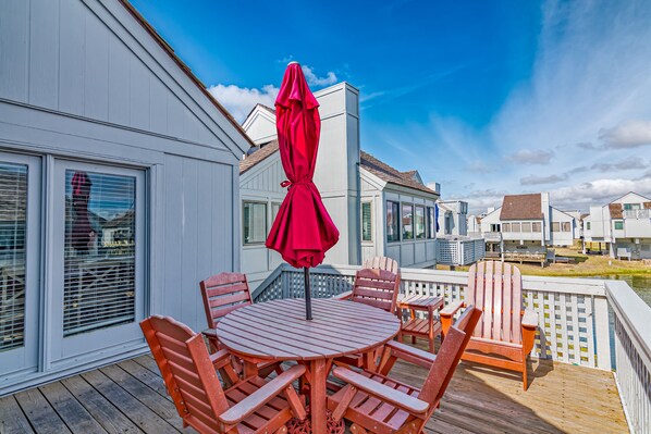 A wooden deck with a round table and chairs, a red umbrella, and a view of neighboring houses.