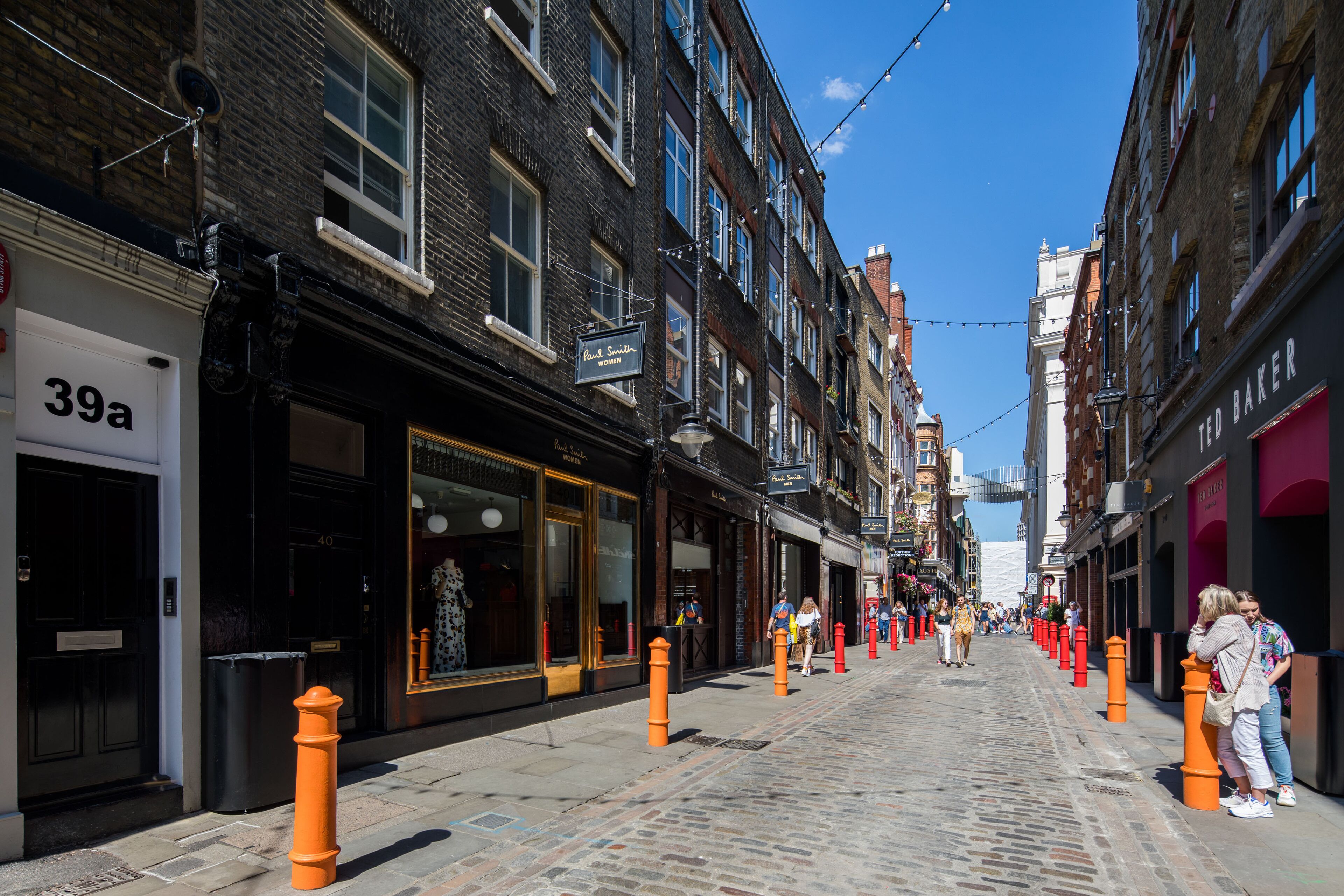 A cobblestone street lined with brick buildings, storefronts, and orange bollards.