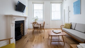 Un salon avec une cheminée, un téléviseur fixé au mur, un canapé et un coin repas avec des chaises.
