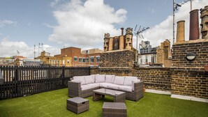 Une terrasse sur le toit avec un canapé d’angle, deux poufs et un mur de briques agrémenté de cheminées.