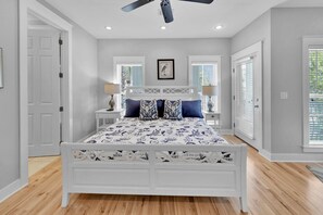 A bedroom with a white bed, two bedside tables, a ceiling fan, and a window with blinds.