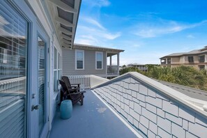 A balcony with two Adirondack chairs, a small trash can, and a white railing.
